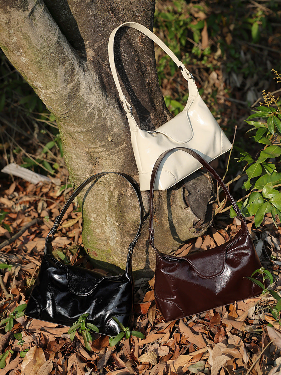 Three cowhide leather shoulder bags in black, coffee, and pearl white displayed outdoors