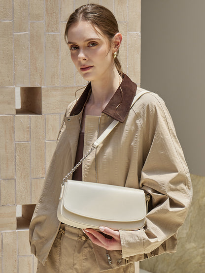 Off-white leather baguette bag worn crossbody against a textured wall