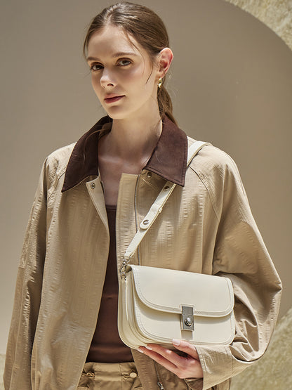 Off-white leather messenger bag held in hand with adjustable strap
