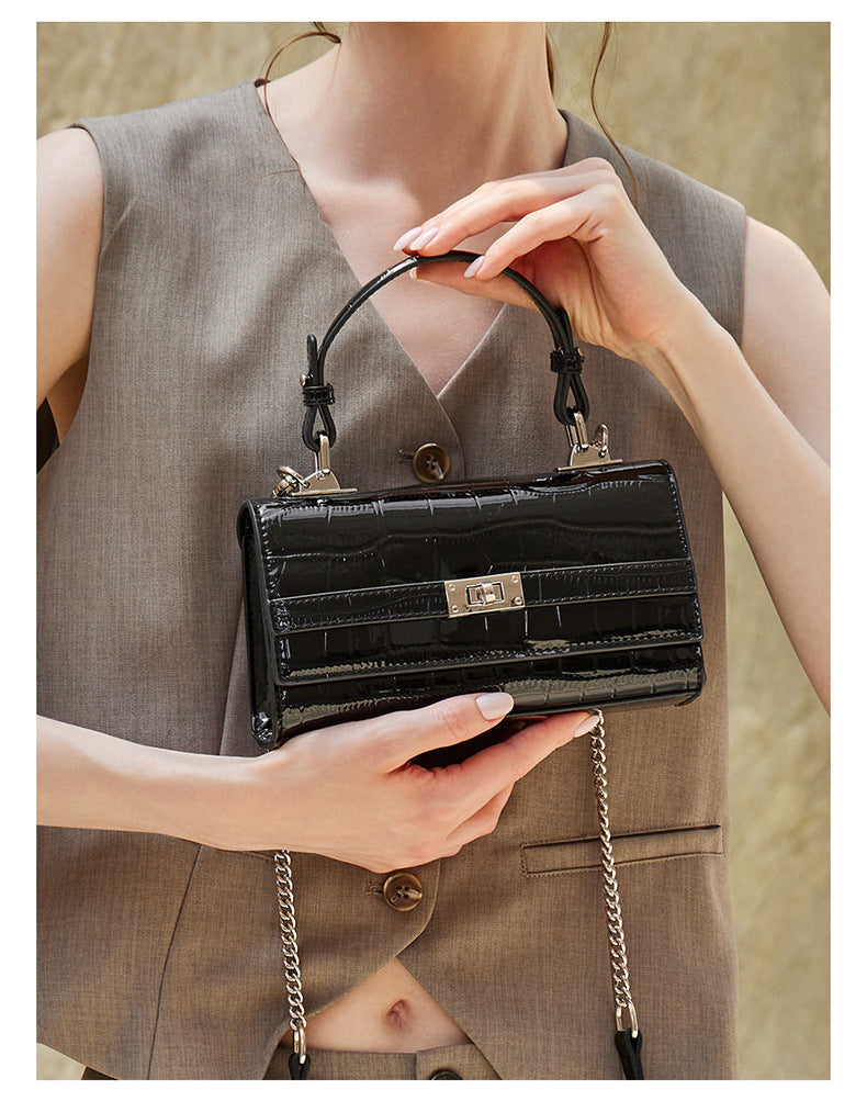 Close-up of hands holding the black croco-embossed bag to show turn-lock closure and handle detail