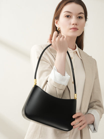 Model carrying the black cowhide shoulder bag by the slim strap against a beige blazer