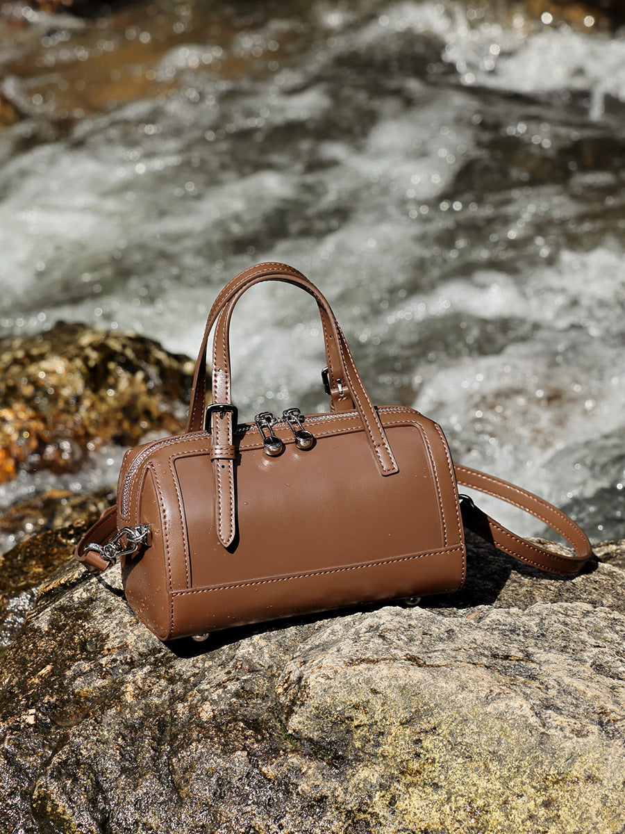 Brown cowhide leather mini Boston bowling bag resting on rocks by a stream
