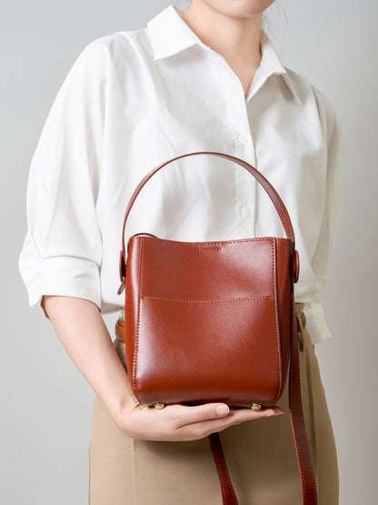 Woman in white shirt holding a brown leather bucket bag by the top handle