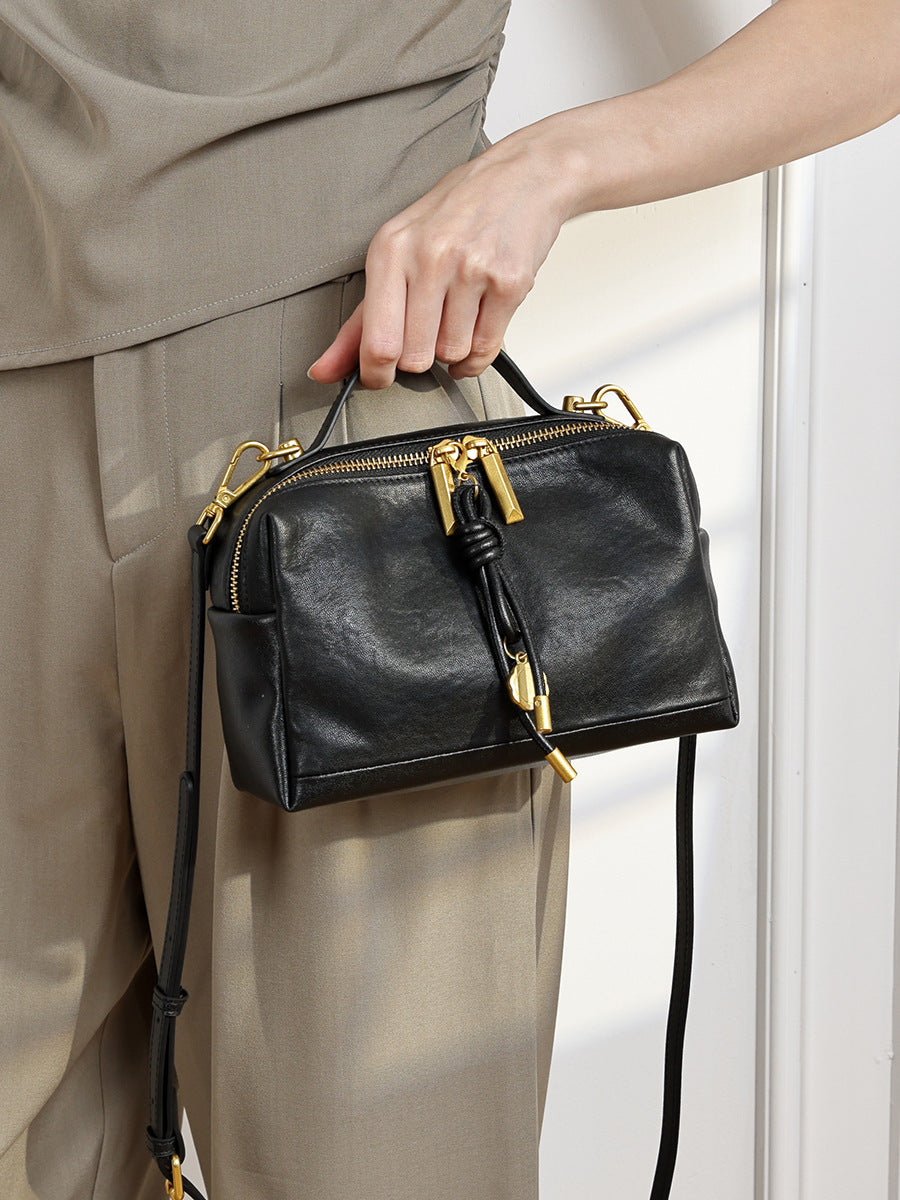Black cowhide leather crossbody bag carried by hand in lifestyle photo