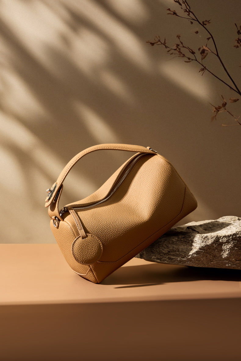 Caramel mini Boston bag propped on stone ledge with branch shadows