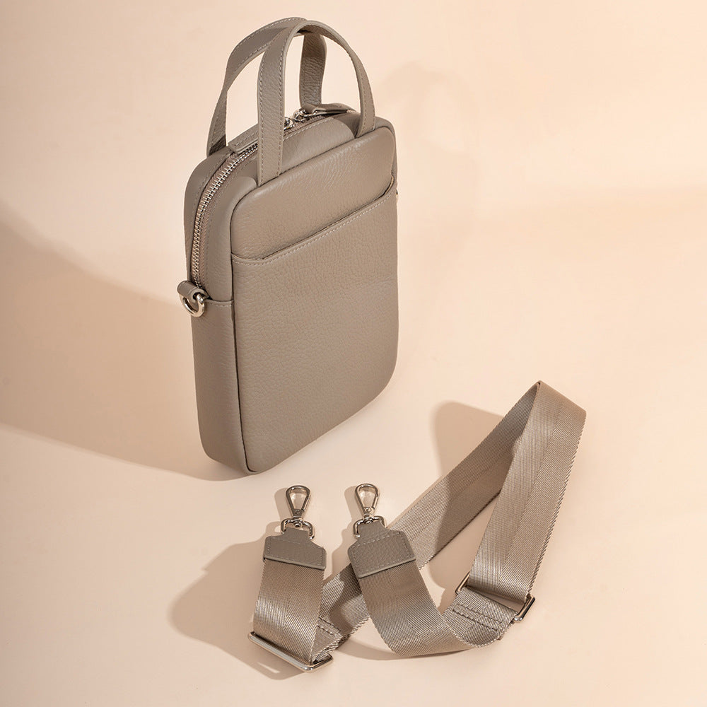 Side angle view of light gray pebbled leather phone bag showing top zip closure and detachable strap