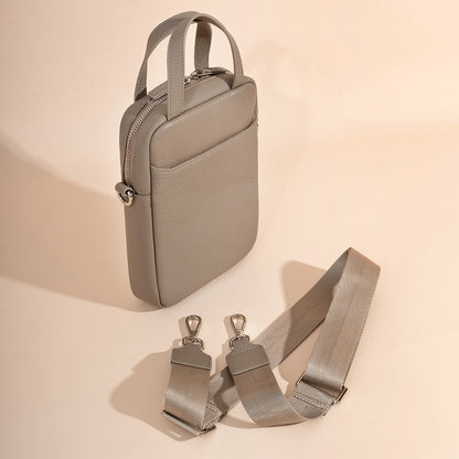 Side angle view of light gray pebbled leather phone bag showing top zip closure and detachable strap
