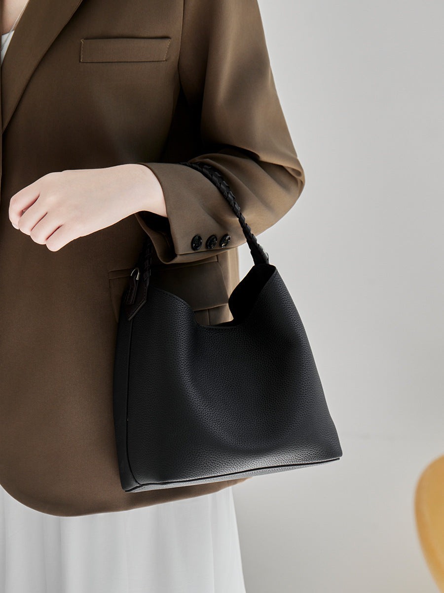 Black leather bucket bag carried by hand against a brown blazer