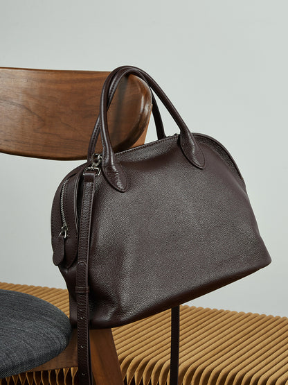 Coffee brown pebbled cowhide bowling tote resting on a wooden chair with woven seat