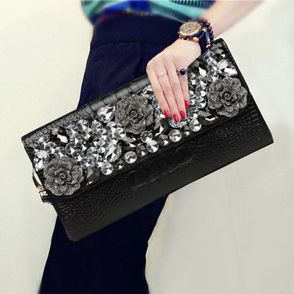 Black embellished leather clutch held by hand, showing crystal-style flap details and rose motifs
