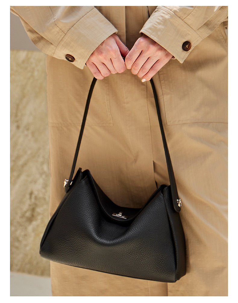 Front close-up of a black pebbled leather hobo bag held by the top handle against beige trousers