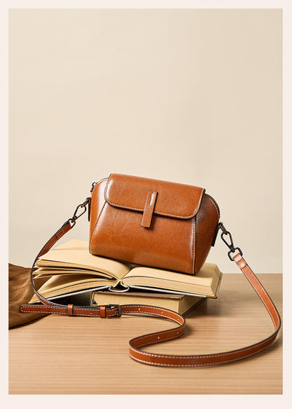 Caramel leather crossbody bag resting on open book on wooden table