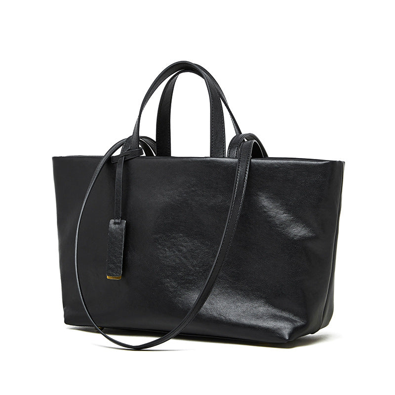 Black cowhide leather tote bag with crossbody strap on white background
