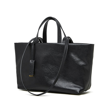 Black cowhide leather tote bag with crossbody strap on white background