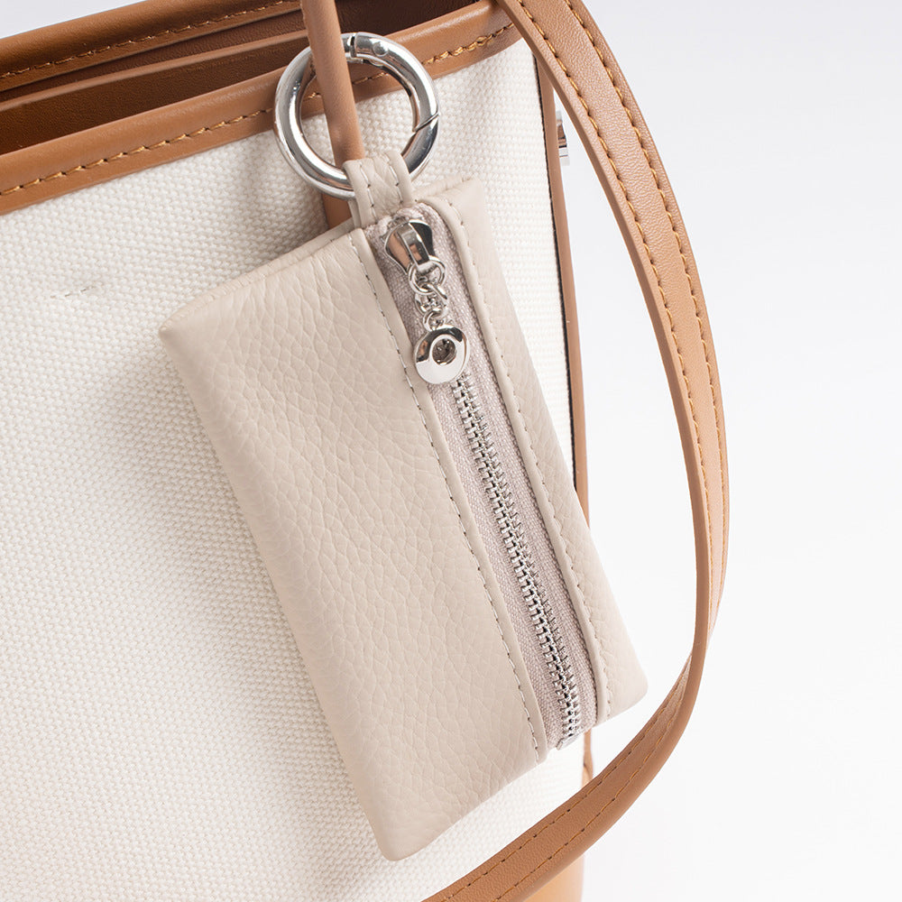 Ivory leather keychain pouch clipped to the strap of a canvas tote bag