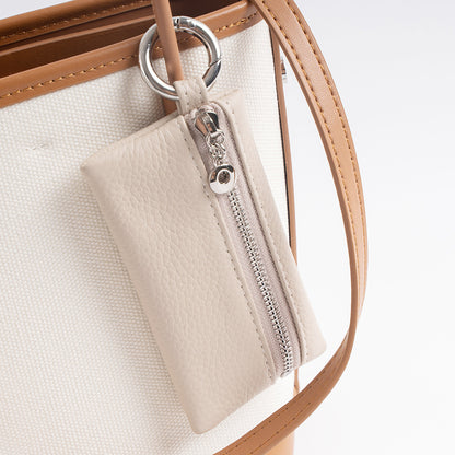 Ivory leather keychain pouch clipped to the strap of a canvas tote bag