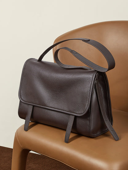 Dark brown leather messenger bag on chair showing back view and strap construction