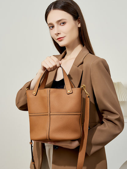Model holding brown leather bucket bag featuring gold-tone hardware