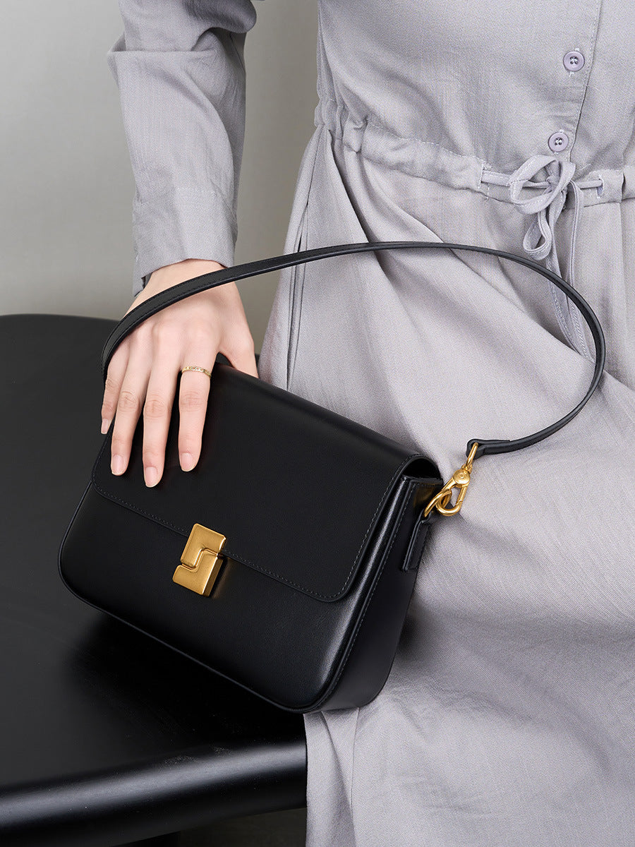 Black cowhide leather crossbody bag held by model in gray dress