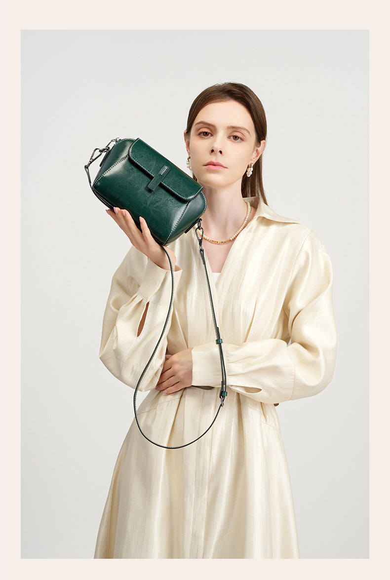 Model in cream shirt holding a deep green leather crossbody bag