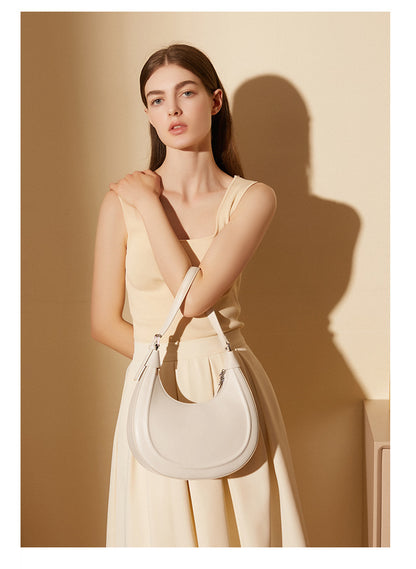 Model carrying a cream white crescent bag as a crossbody with a dress