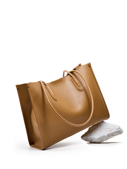 Golden brown leather tote bag displayed at an angle on a stone prop
