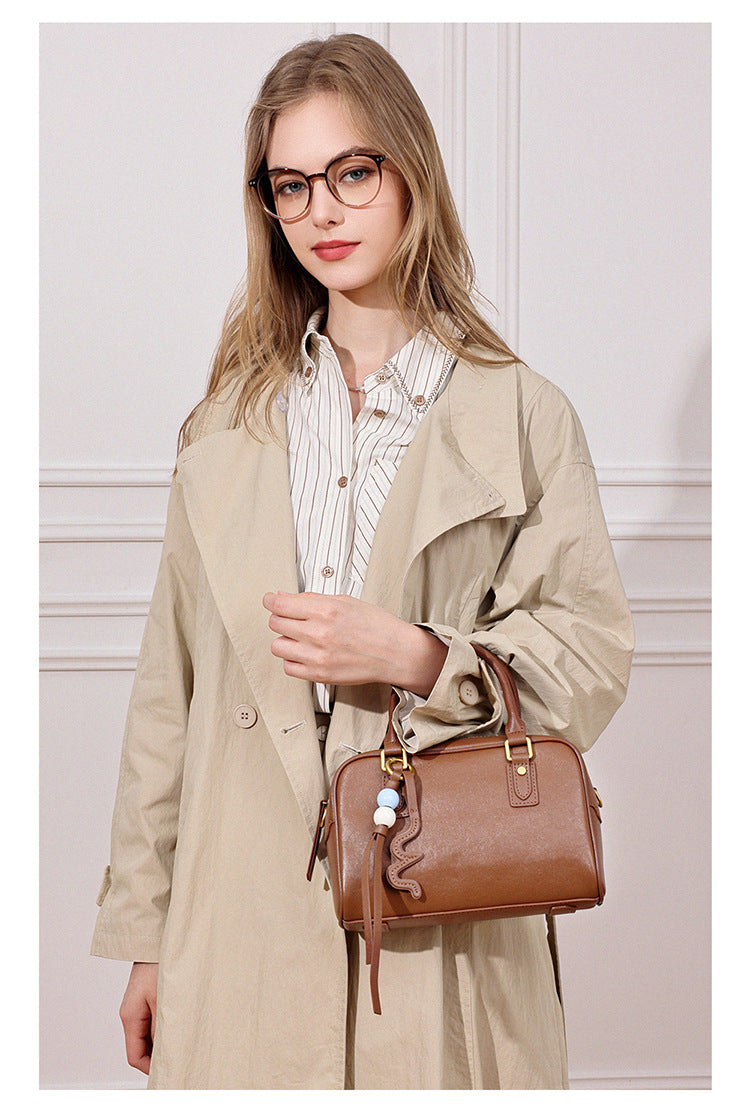 Model in a beige trench coat carrying a caramel brown leather pillow bag by hand