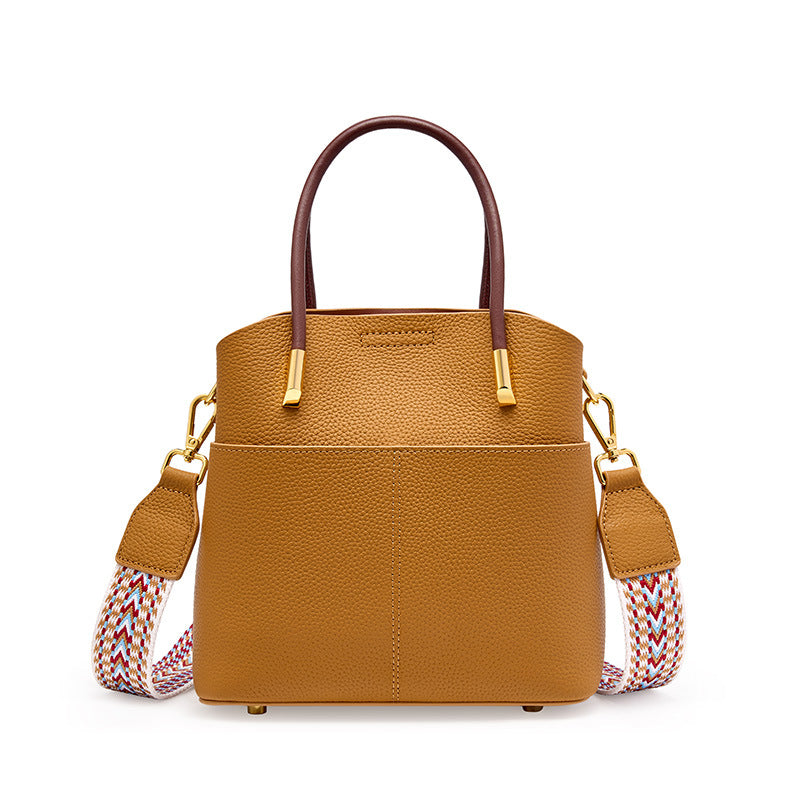 Brown cowhide leather bucket bag with top handles and woven strap on white background