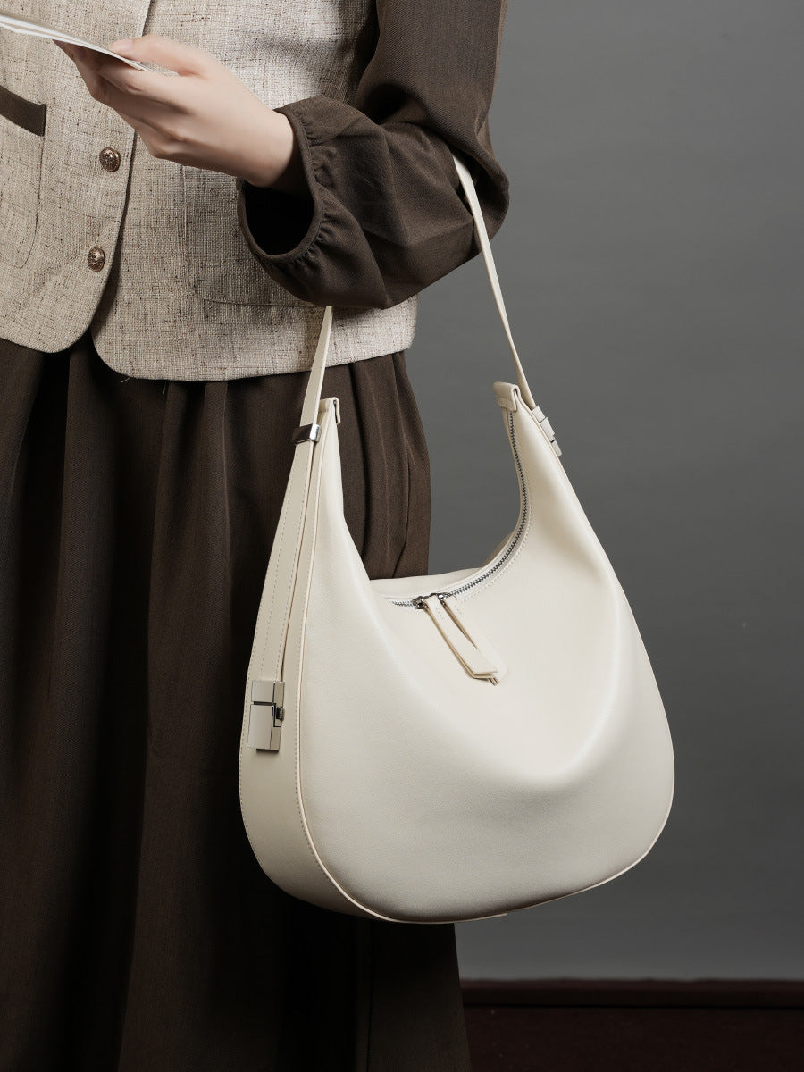 Close-up of the cream white cowhide leather crescent hobo bag held by the strap, showing top zip and square buckle hardware