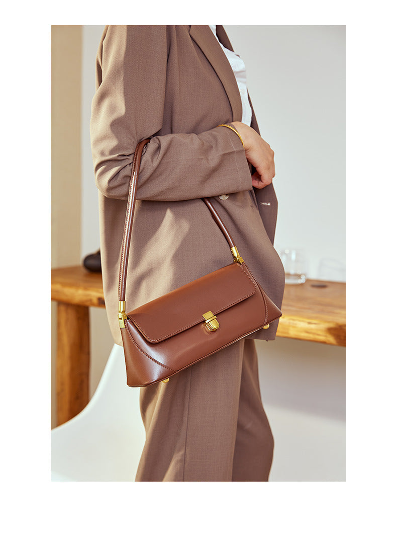 Coffee leather baguette bag held at side in soft indoor lifestyle shot
