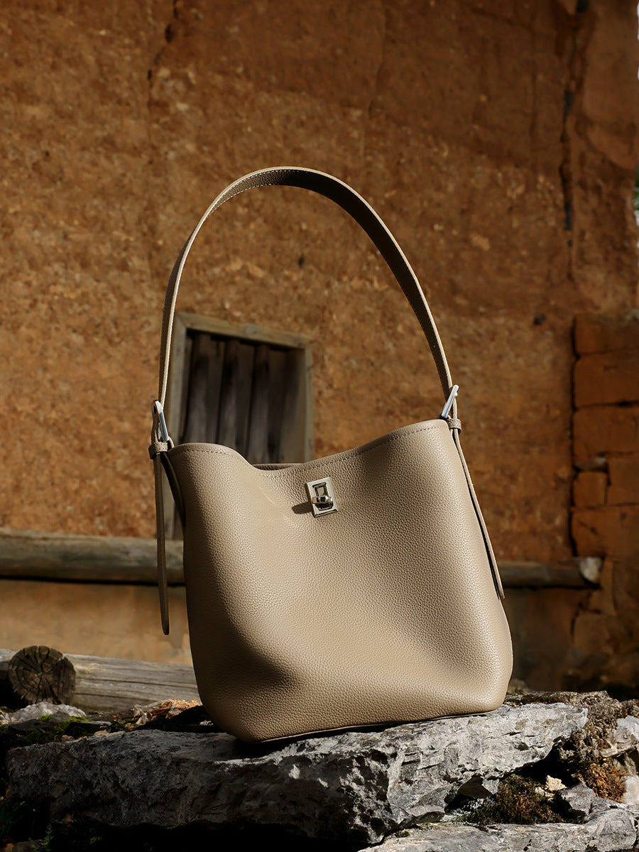 Khaki leather bucket bag resting on rustic stone and wood outdoors