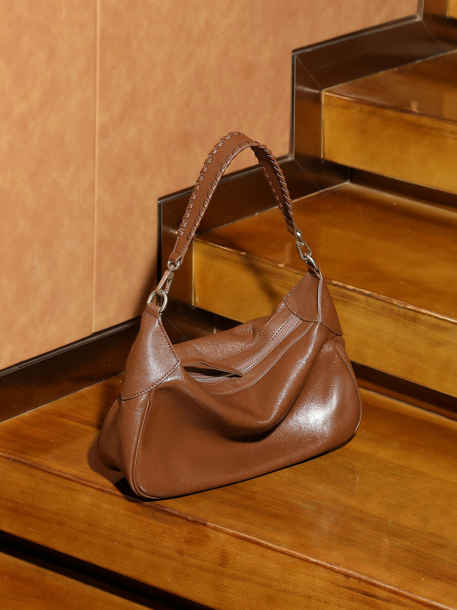 Brown leather hobo bag with braided strap displayed on wooden steps