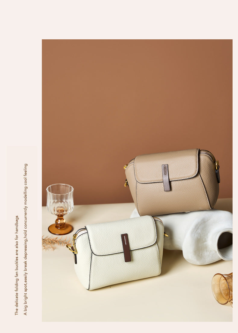 Khaki and ivory shell crossbody bags styled on cream pedestals with amber glassware