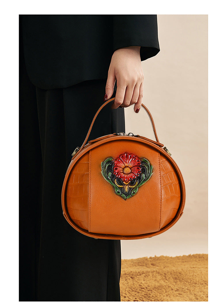 Brown round bag carried by the top handle, showing its curved silhouette