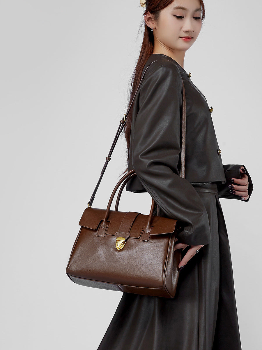 Dark brown leather satchel bag worn crossbody with adjustable strap