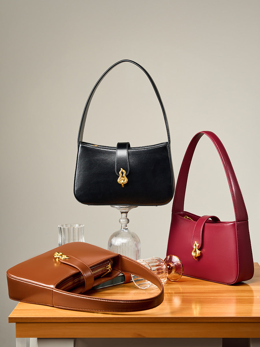 Three colorways of leather shoulder bags styled on wooden table with glassware