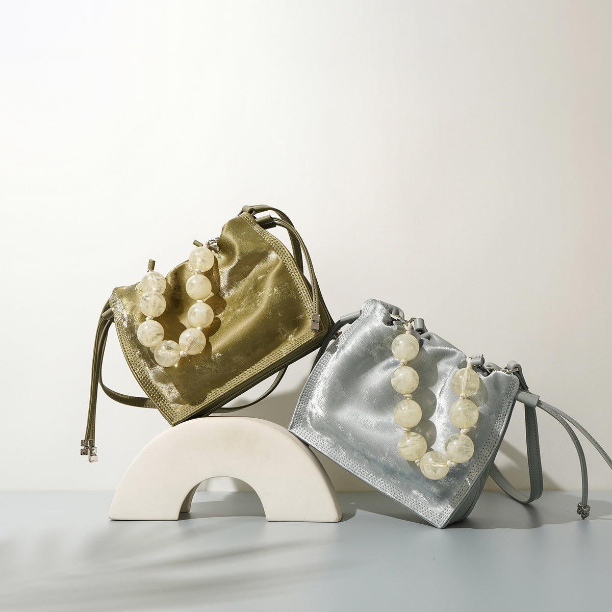 Champagne and silver mini bucket bags styled together on a curved display