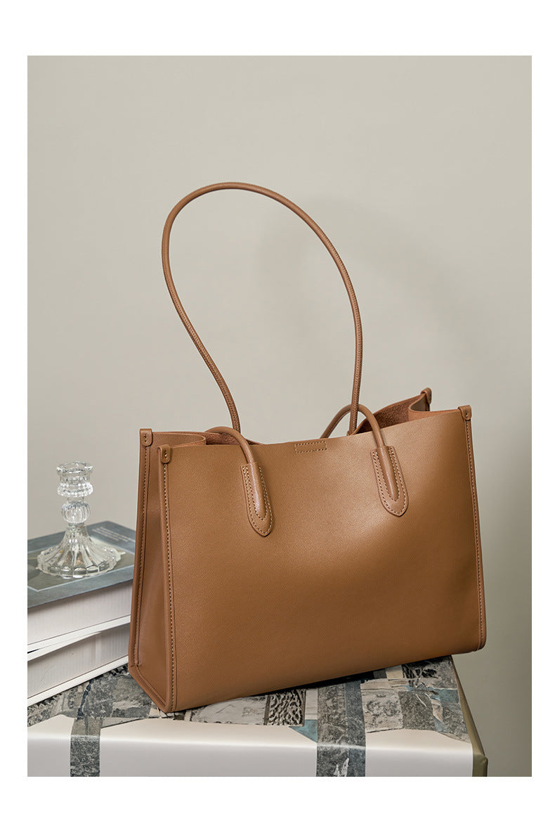 Golden brown leather tote bag styled on stacked books with a crystal perfume bottle