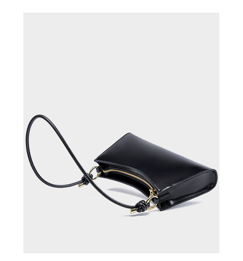 Black leather shoulder bag with strap laid flat showing top zip closure