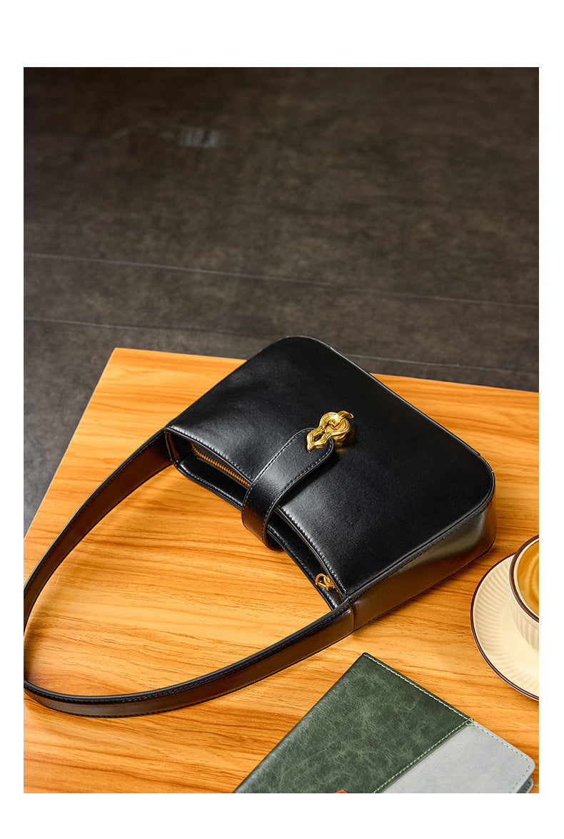 Black leather shoulder bag flat-lay on wooden table with notebook and coffee cup
