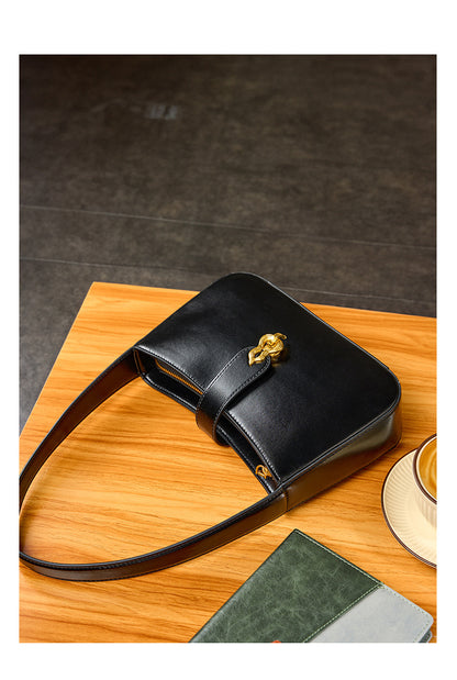 Black leather shoulder bag flat-lay on wooden table with notebook and coffee cup