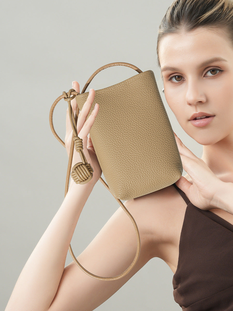 Beige pebbled cowhide mini bucket phone crossbody bag held against the shoulder by a model