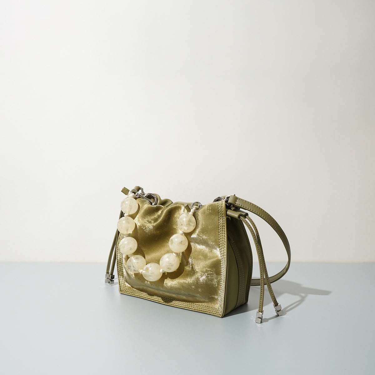 Side angle of champagne mini bucket bag showing drawstring and dual leather straps