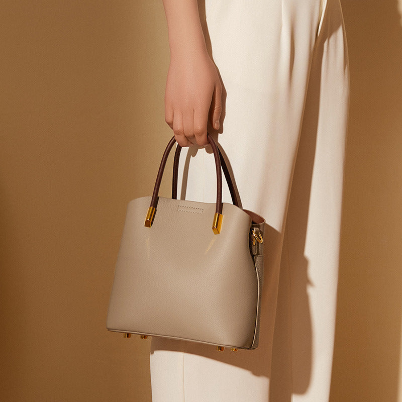 Gray bucket bag carried by the top handles against a cream dress