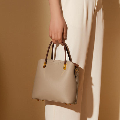 Gray bucket bag carried by the top handles against a cream dress