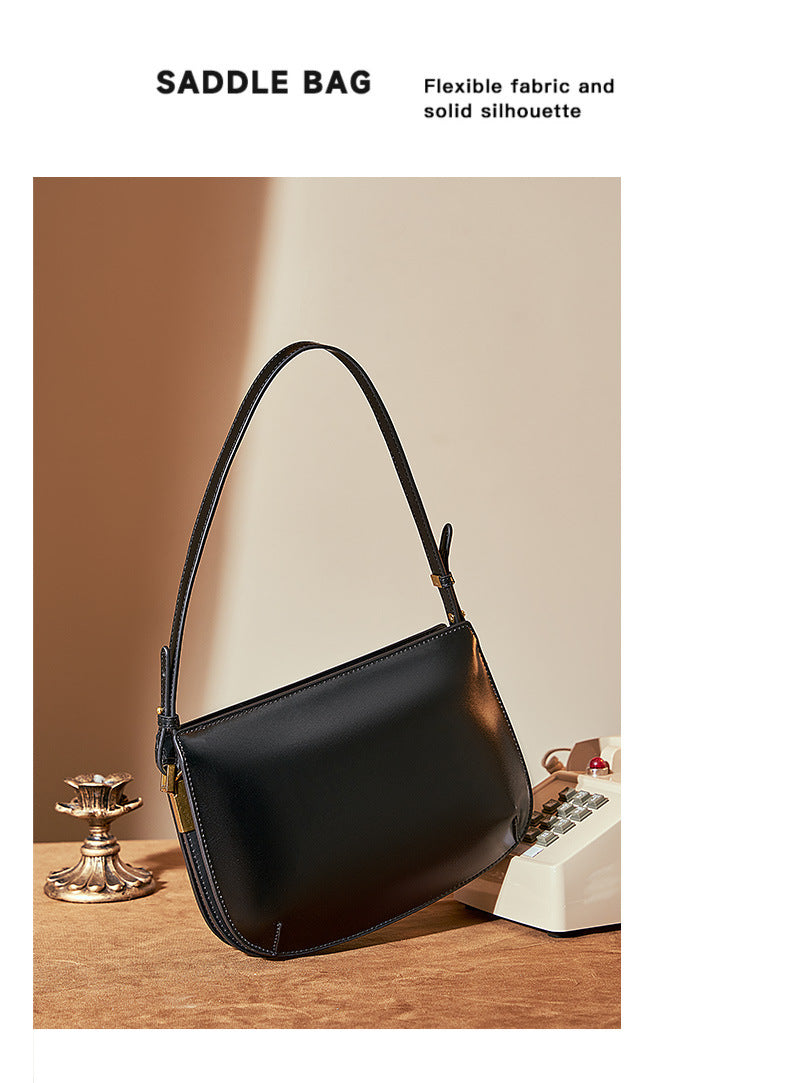 Black leather underarm bag on a brown surface beside a vintage telephone, Saddle Bag graphic