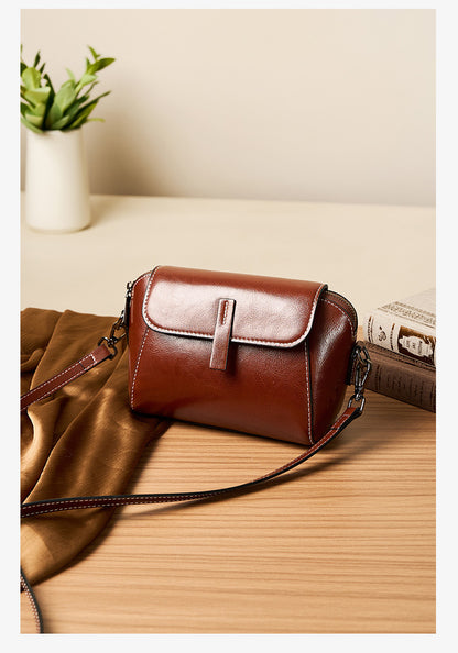 Brown oil-wax leather crossbody bag displayed on a wooden surface with scarf and books