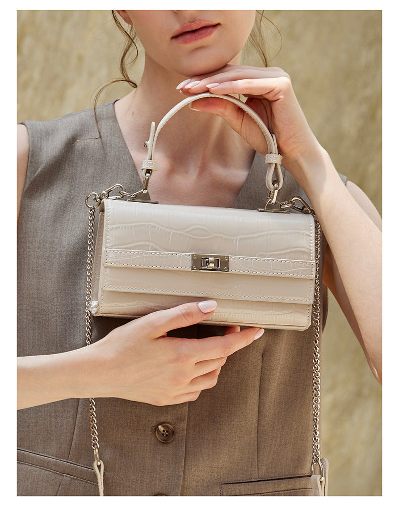 Close-up of hands holding the cream white croco-embossed bag showing the turn-lock and top handle