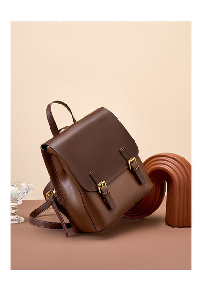 Dark brown leather backpack shown from a side angle on a terracotta surface with decorative objects