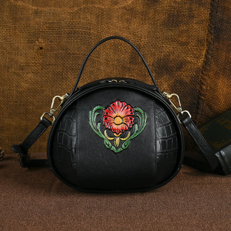 Black round crossbody bag featuring a colorful floral front accent